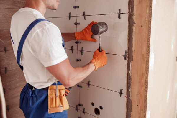 Male worker installing ceramic wall tile in house Close up of young man construction worker using rubber hammer while placing tile on the wall